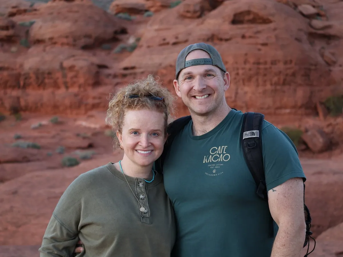 Josh and Steph smiling together in front of red sandstone cliffs in southern Utah.